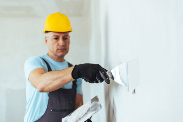 Plasterer in blue working uniform plastering the wall indoors